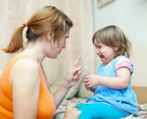 Woman berates crying baby at home interior. Focus on child only